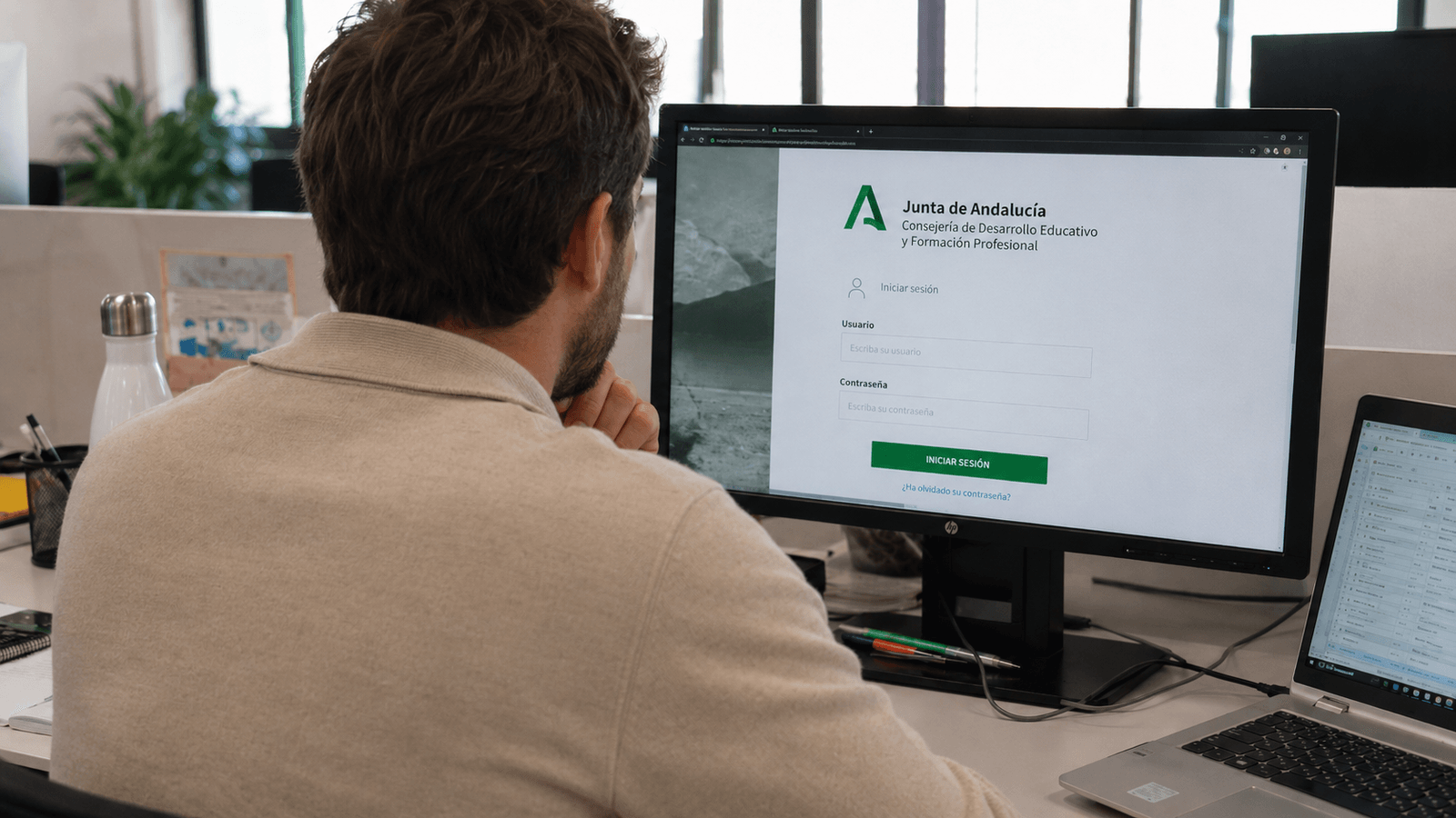 Usuario accediendo al portal de la Junta de Andalucía desde un ordenador en una oficina, con su portátil al lado..